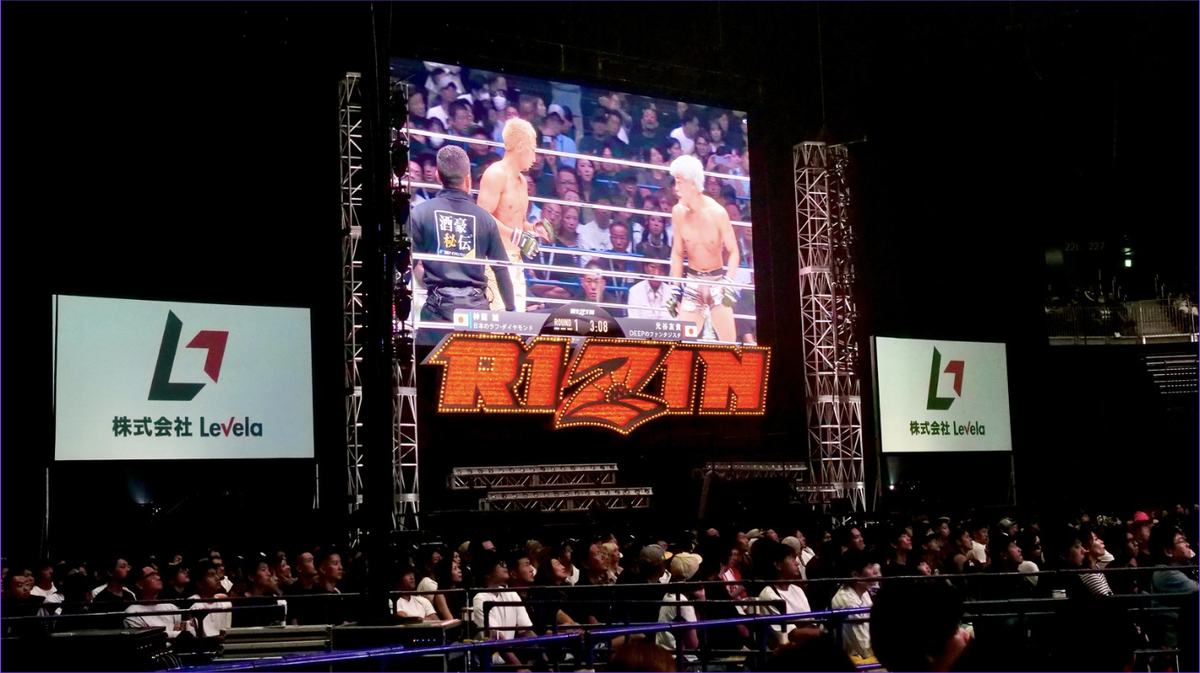 RIZIN会場の大型ビジョンと株式会社Levelaのスポンサーボード